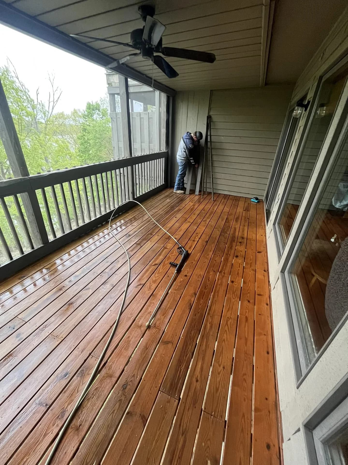 Worker pressure washing a screened porch with freshly cleaned wood flooring